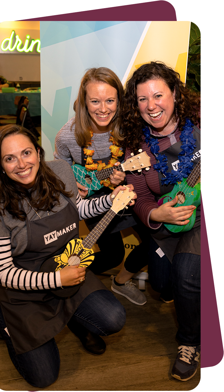 Group of women holding hand-painted ukuleles in Yaymaker aprons.